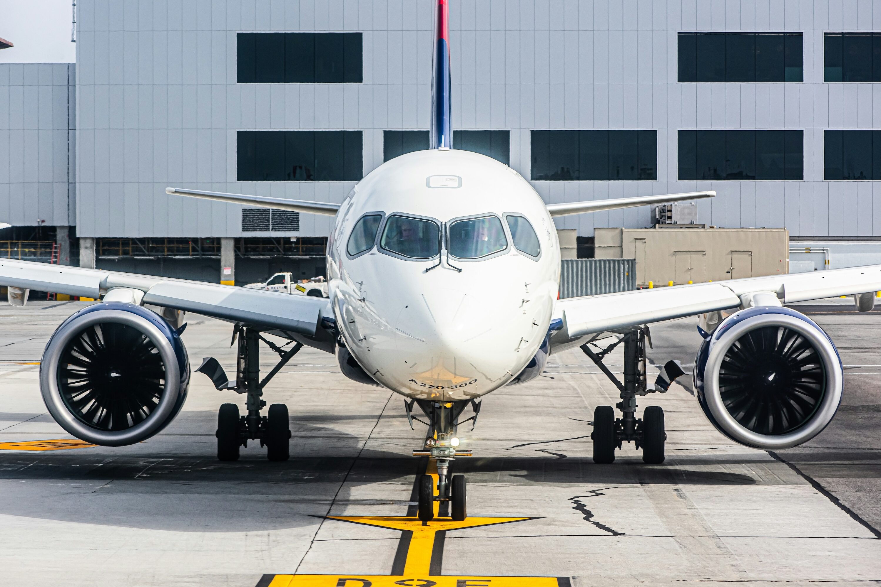 An Airbus A220 taxiing in to a gate, viewed from head-on.