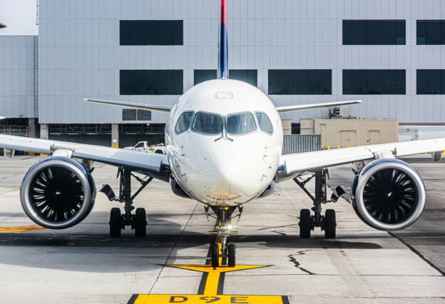 An Airbus A220 taxiing in to a gate, viewed from head-on.